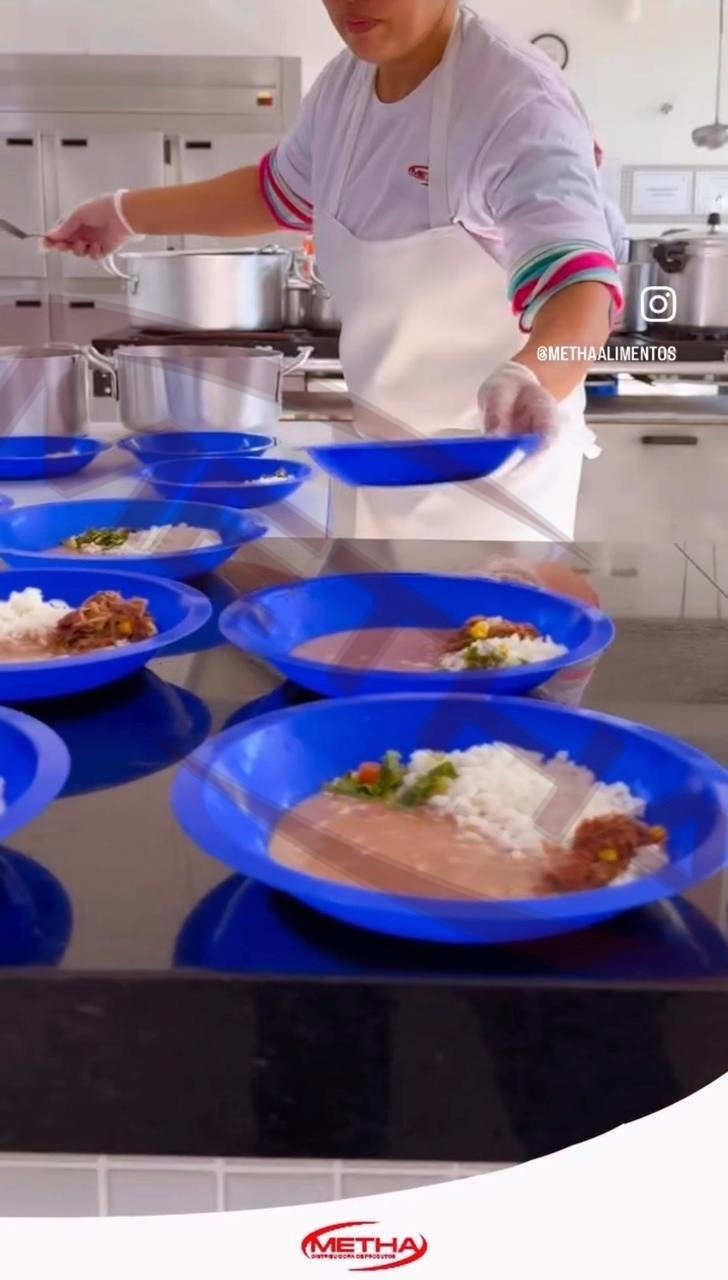 Funcionária Metha servindo refeições coletivas em pratos